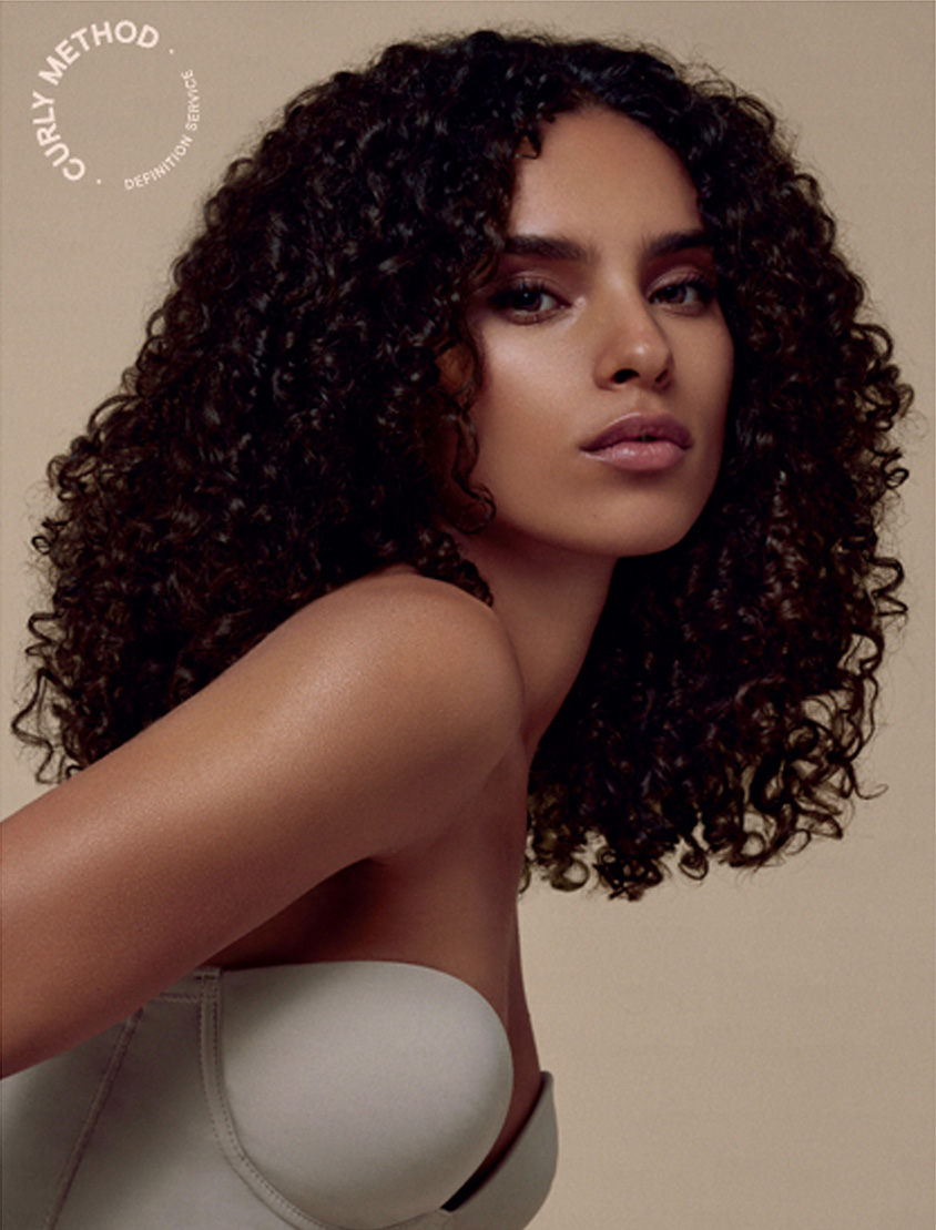Portrait of a woman with stunning curly hair and natural makeup against a neutral background.